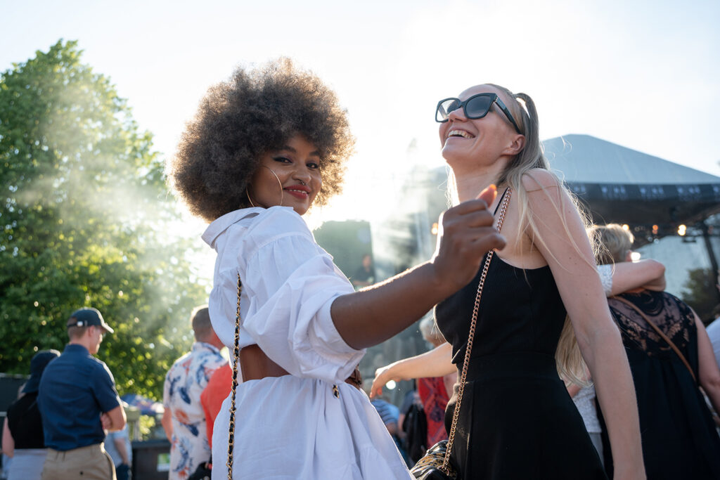 Kaksi naista tanssii kesäiltana festareilla.