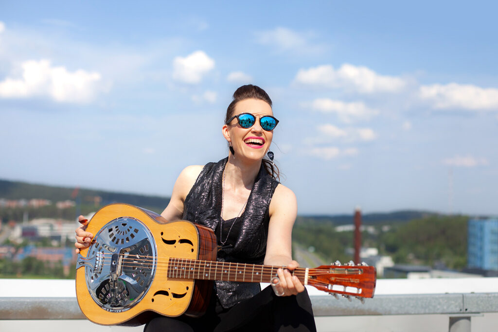 Nainen istuu katolla soittamassa kitaraa. Taustalla näkyy Puijon torni.
