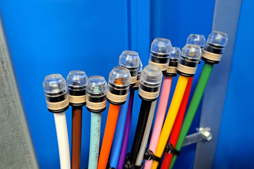 Erivärisiä kuituputkia rivissä sinistä seinää vasten.