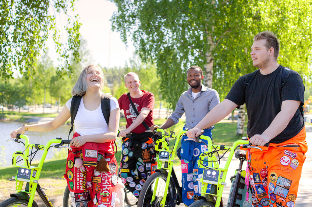 Neljä iloista, haalariasuista opiskelijaa on liikkeellä Vilkku-fillareilla.