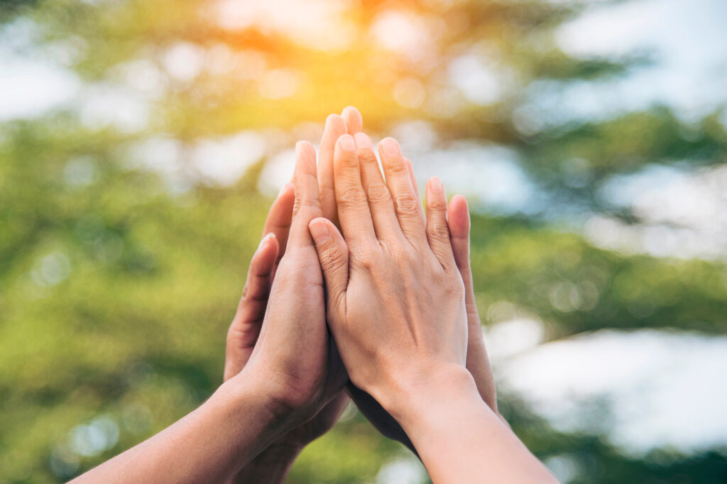 Monen ihmisen kädet yhdessä ilmassa kesäisenä päivänä.