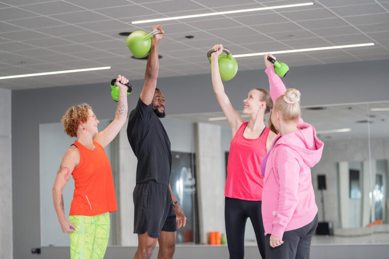 Neljä henkilöä nostaa kahvakuulia jumppasalissa.