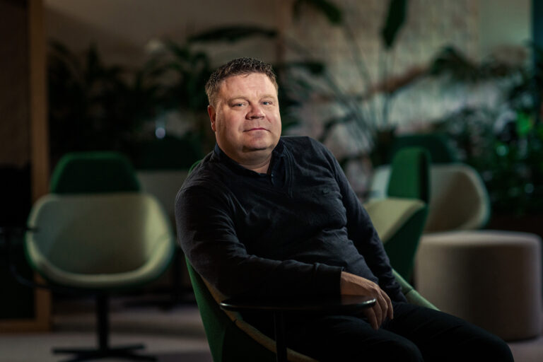 Mies istuu cowork-tilassa ja katsoo kameraan.