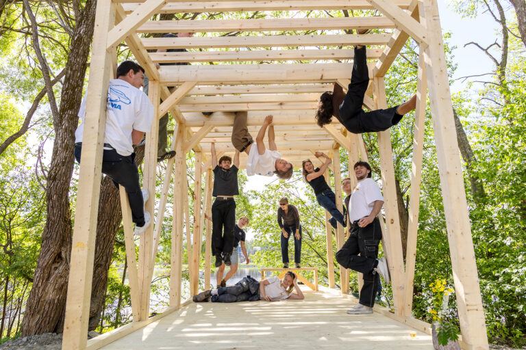 Opiskelijat kiipeilevät puurakennelmassa järven rannalla.